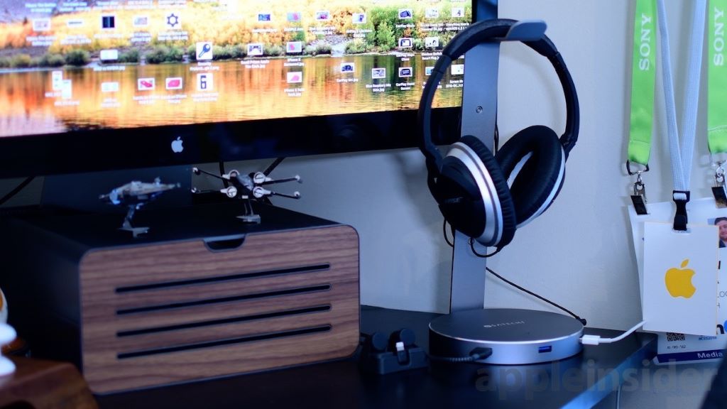 Headphones hanging on a desk-mounted headset holder beside a computer monitor